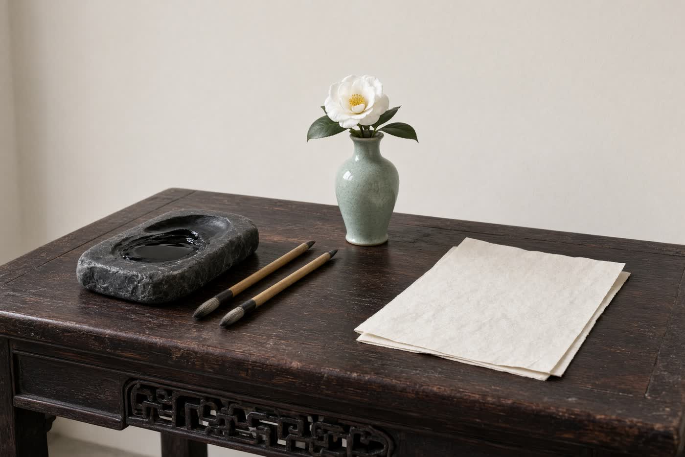 A Qing writing table in daylight: inkstone, brush, a small vase with a single camellia, no faces.